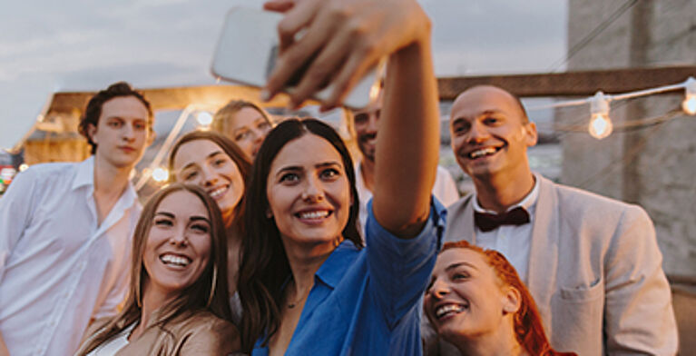 Eine Gruppe an Menschen machen in Feierlaune ein Selfie auf der Terrasse. (c) AleksandarNakic