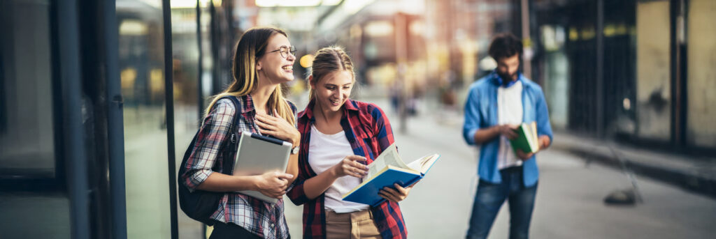 Zwei Schülerinnen, einander zugewandt mit ihren Schulunterlagen in der Hand
