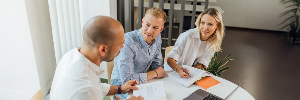 zwei männliche und eine weibliche Studierende sitzen gemeinsam an einem Tisch und lernen